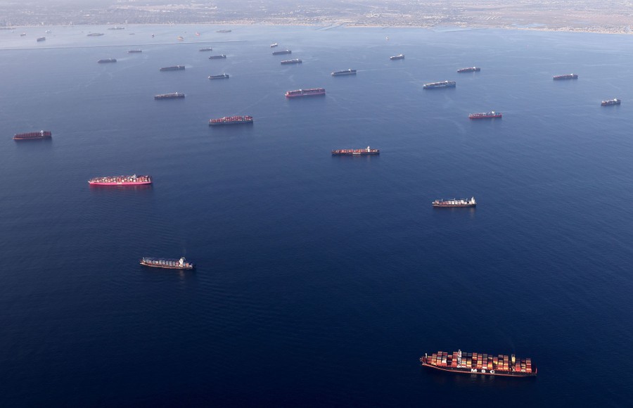 Dozens of container ships sit anchored offshore.