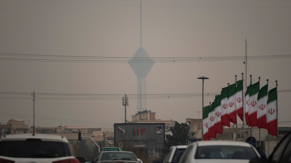 A hazy photograph of a street in Iran with a large skyscraper in the background and a number of Islamic Republic flags in the foreground