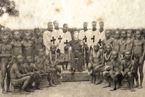 A black-and-white photo of a white man sitting among a group of Andamanese men