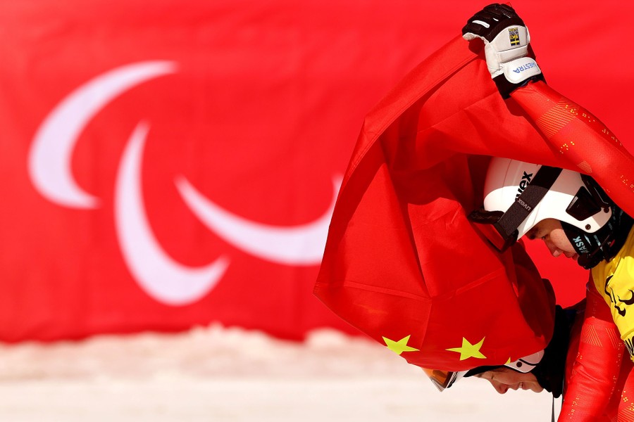 A pair of athletes hold a Chinese flag above their heads.