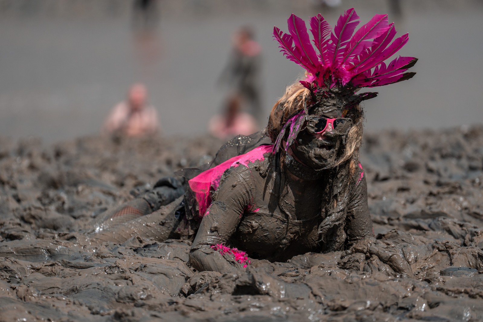 A woman in costume, covered in mud, crawls across a muddy plain.