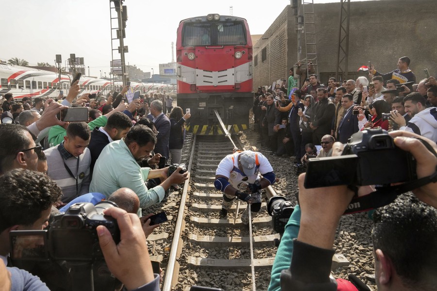 A crowd watches as a man pulls a locomotive down a track, using a thick rope.