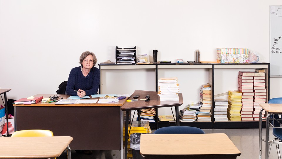 An English teacher sits at a desk in an empty high school classroom