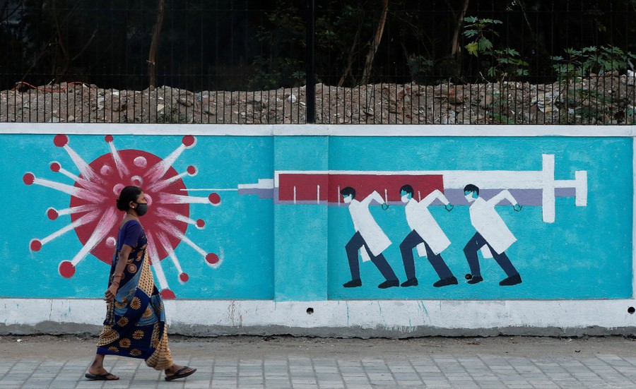 A woman walks past a mural of a vaccine dose being delivered to a virus.