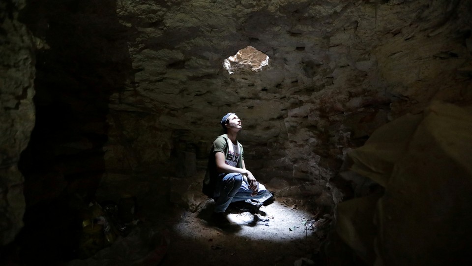 A man looks up through a hole at the top of a cave.