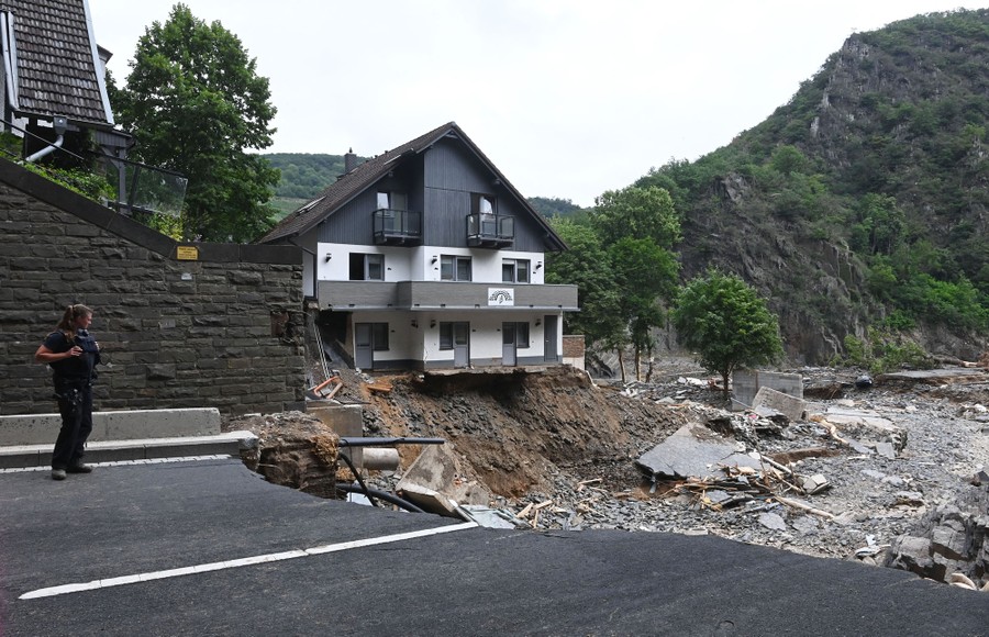 A damaged house stands beside a washed-out roadway.