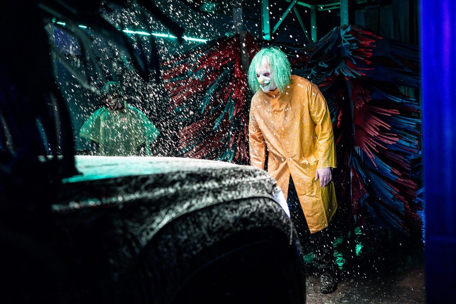 Two people dressed as scary clowns menace a car as it passes through a car wash.