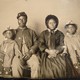 A Black Civil War soldier and his family sit for a portrait in formal clothes.