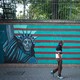 A man in front of an anti-U.S. mural featuring the Statue of Liberty, the American flag, and a map of Iran in barbed wire