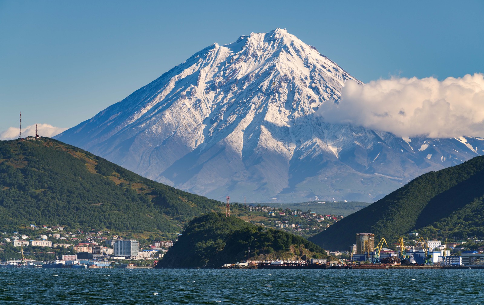 A view of a port city backdropped by a tall snow-capped volcano