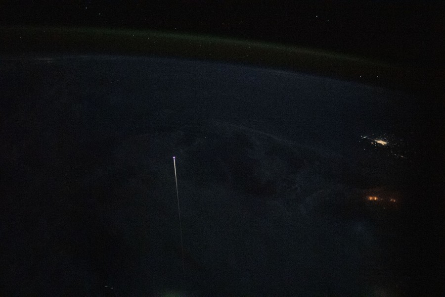A small streak of light is seen above the night side of the Earth.