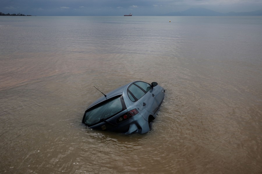 A small car is half-submerged in muddy water in a bay.