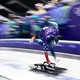An Olympic athlete sprints on an ice track, bent over, pushing a small sled at the start of a run, legs and arms blurred by motion.