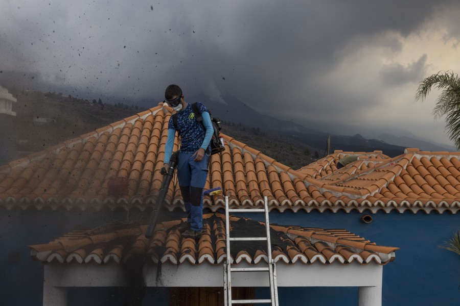 A person uses a blower to move ash from the tiled roof of a house.