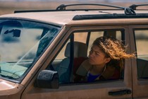 Zendaya as Rue sticks her head out of the driver's side window of a dirty car.