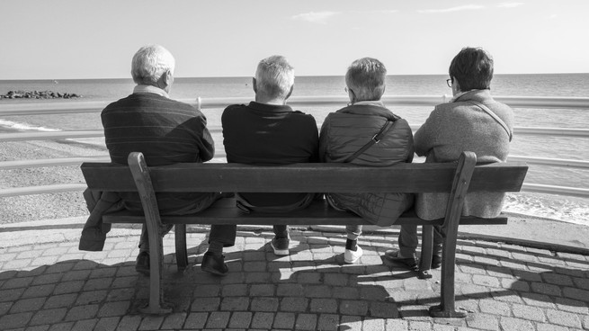 A group of elderly people sit on a bench, looking at the ocean