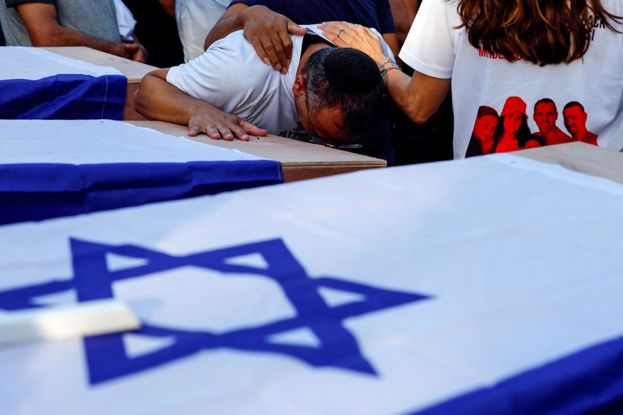 People mourn and lean close to several caskets draped with Israeli flags.