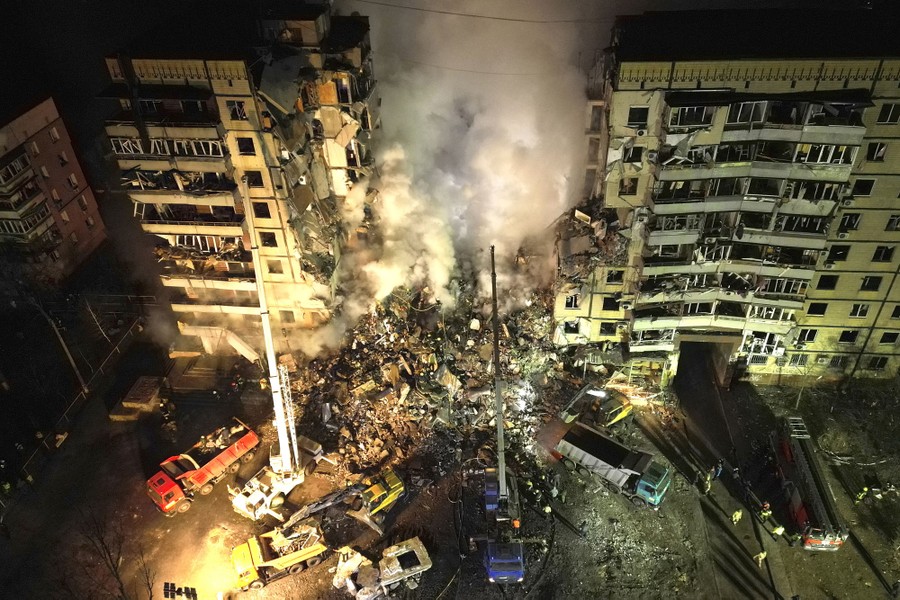 Emergency workers clear rubble from a large residential building, partially collapsed after a missile strike.