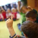 An unrecognizable kindergartener raises his hand