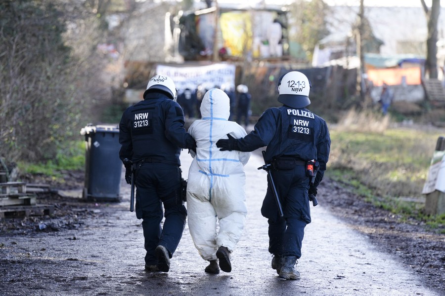 Riot police escort a detained protester dressed in white protective gear.
