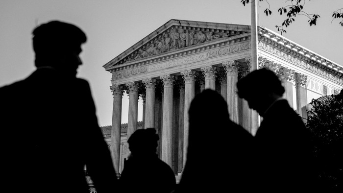 Three shadowy figures in front of the Supreme Court