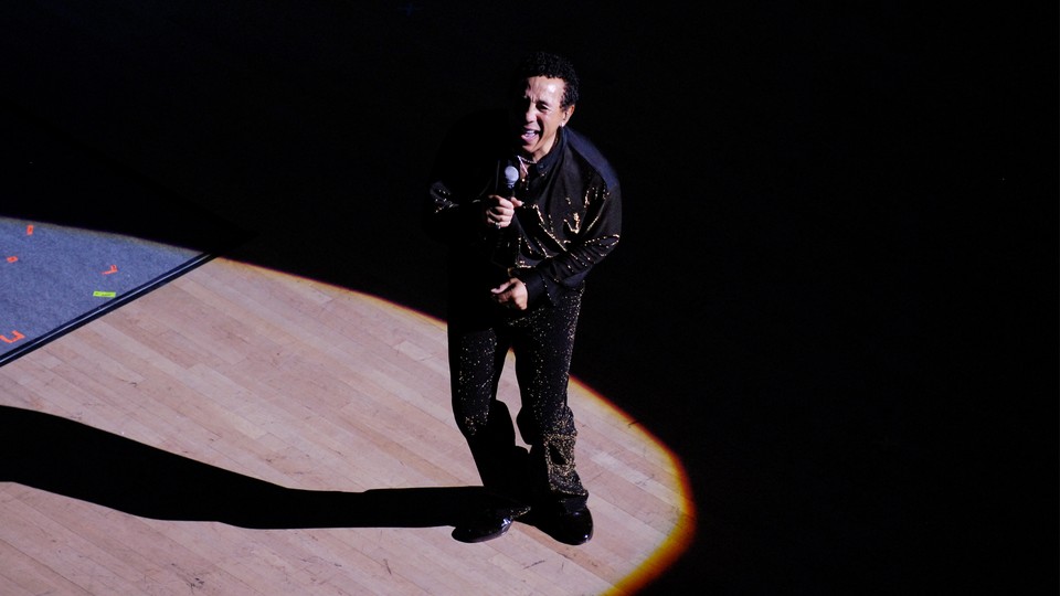 Smokey Robinson performing on a dance floor inside a bright spotlight