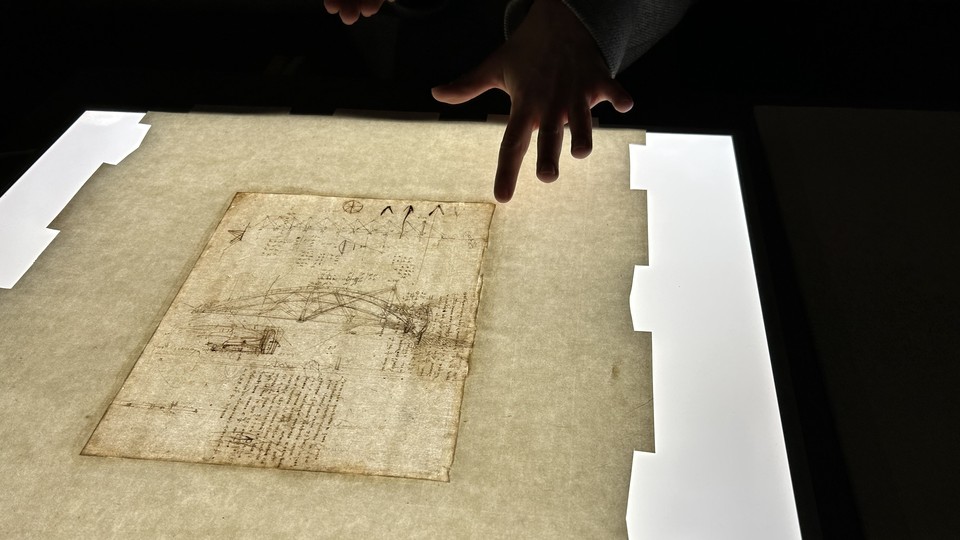 A hand points to a light box with a Da Vinci drawing