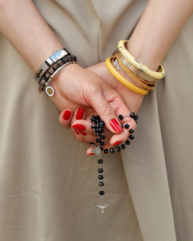 Color photo of a woman holding a rosary with her hands draped behind her back.