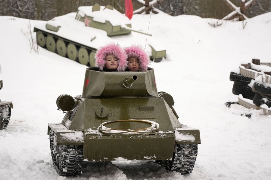 Two children ride in a scale model of a World War II-era Soviet tank in a snowy park.