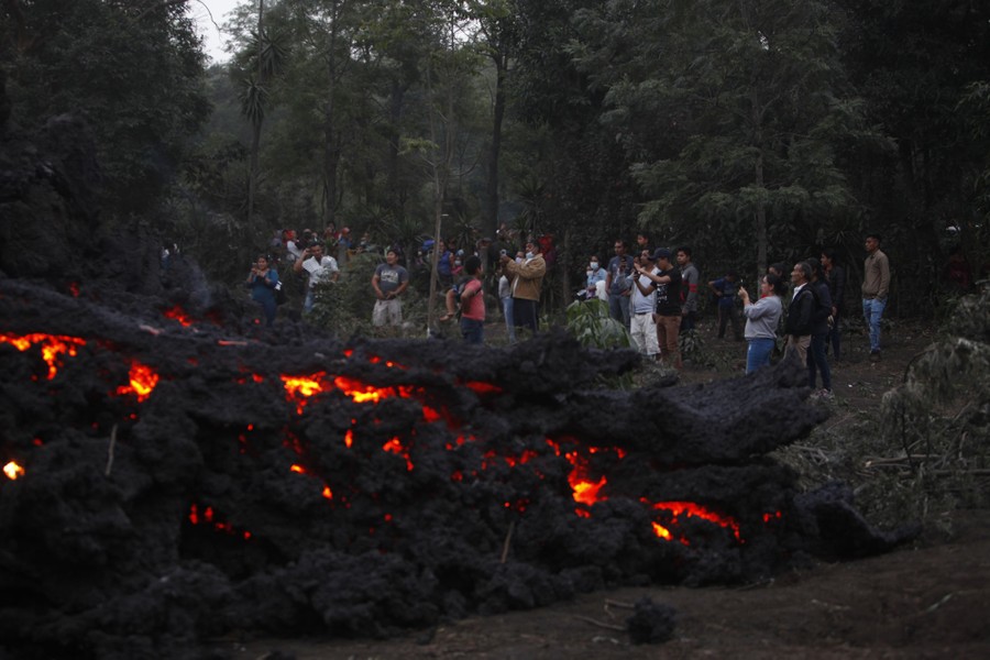 A crowd of people gather near slow-flowing lava.