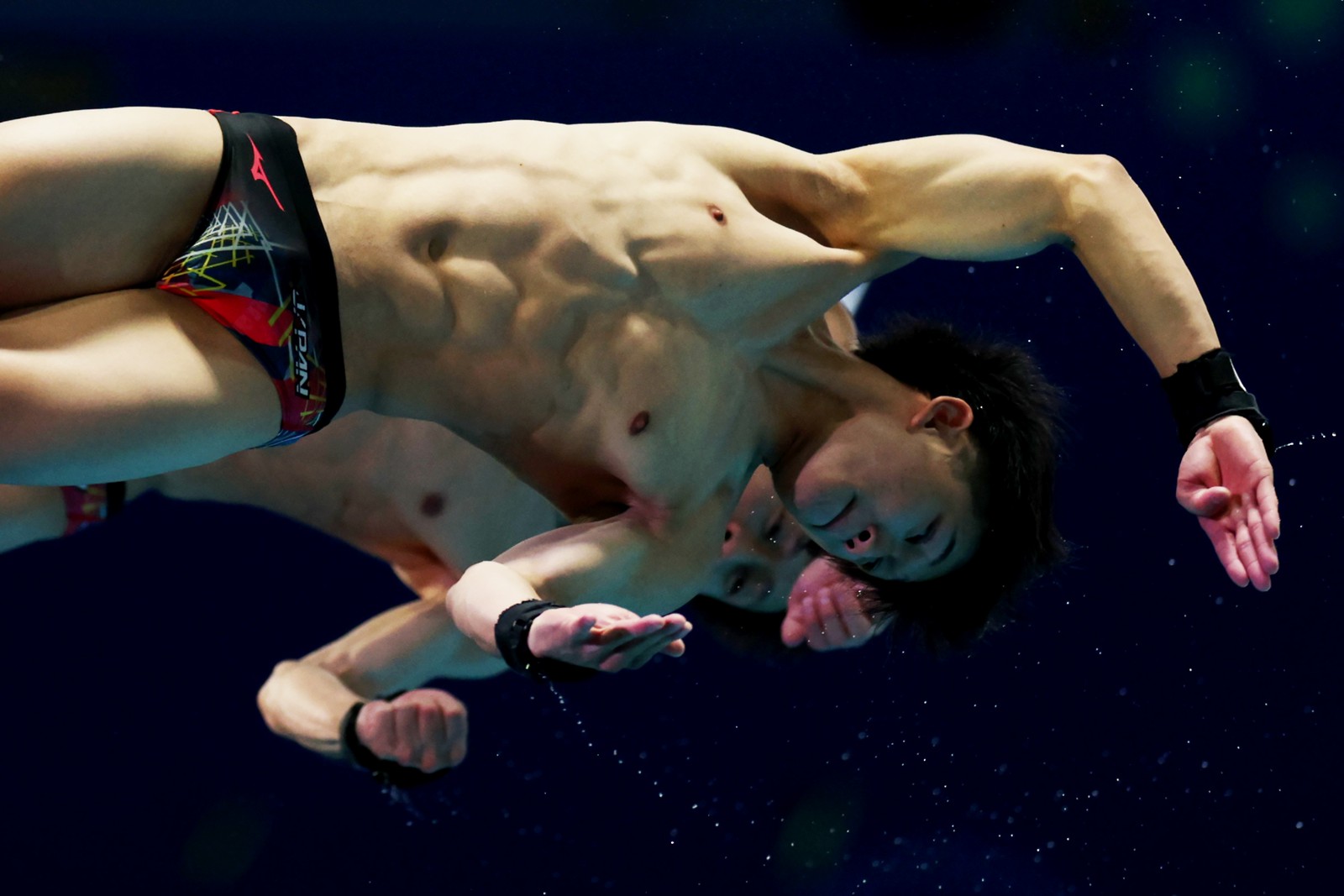 A pair of synchronized divers, scene twisting in midair.