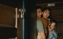 Jonathan Groff, Ben Aldridge, and Kristen Cui hide behind a cabin door in "Knock at the Cabin."