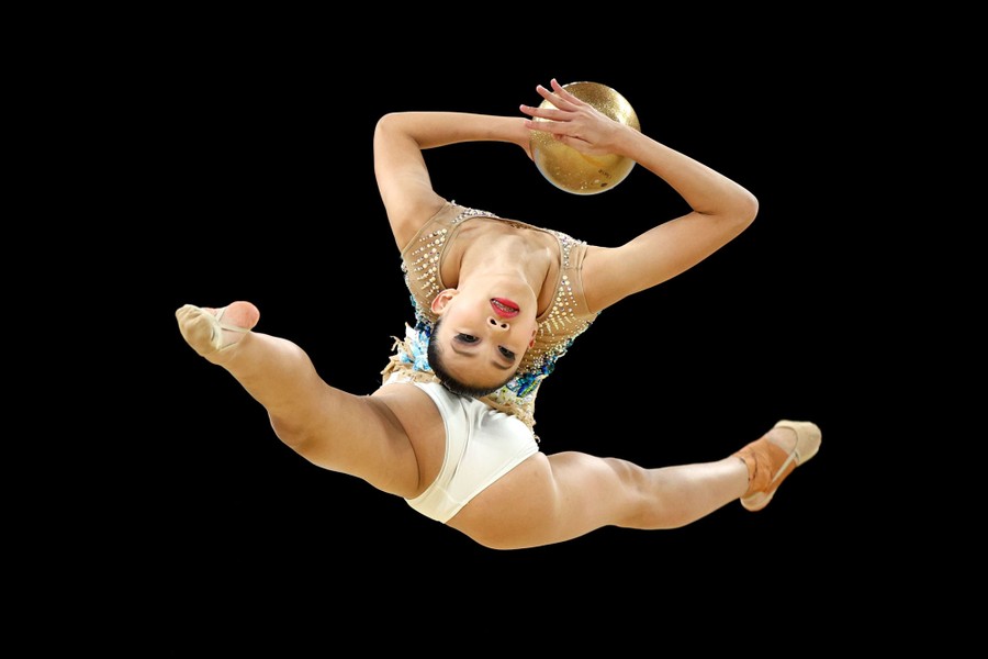 A gymnast performs a high leap while holding a ball.