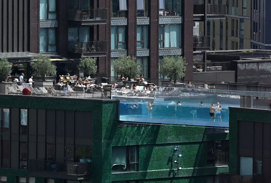 People swim in a clear, suspended swimming pool bridge.