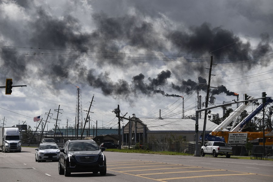 Cars and trucks drive past a storm-damaged industrial area.