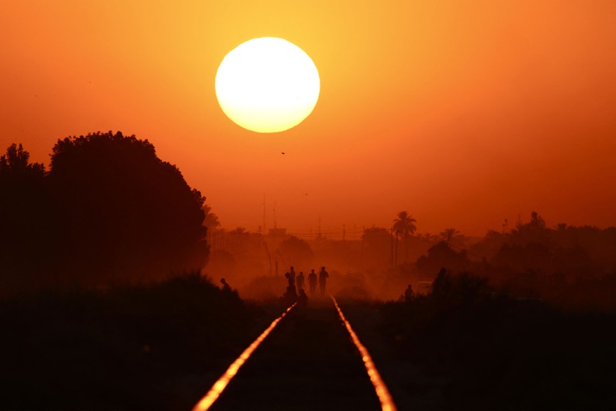 Several people walk along railroad tracks beneath a setting sun.