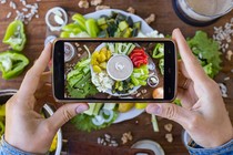 A person uses a smartphone to photograph a platter of vegetables and vegan mayonnaise.