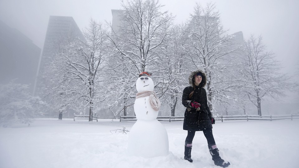 A woman wearing a heavy winter coat walks past a snowman she built in a park during blizzard conditions in Chicago, in 2015. 