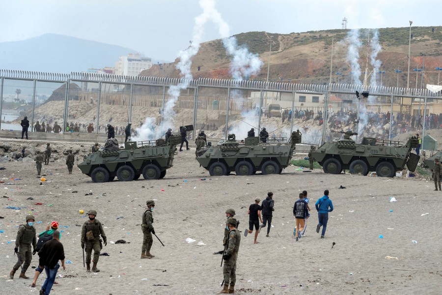 Soldiers and military vehicles stand along a border fence on a beach.