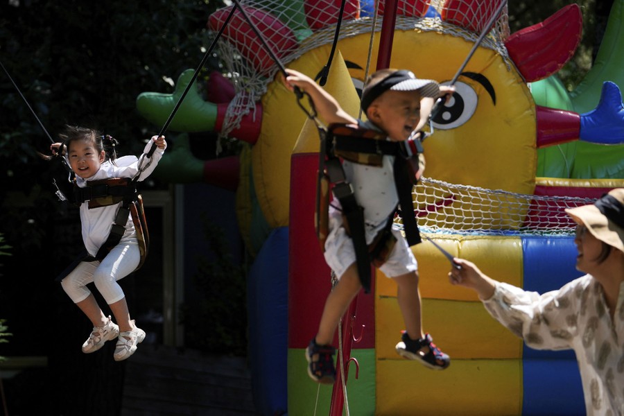 Two young children dangle from harnesses on a ride in an amusement park.