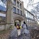 A mother and her son walk hand-in-hand into a brick school building. They are unrecognizable from the back.
