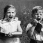 Two children in a field display extreme emotion while holding books.