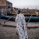 A man on the beach stands near several different-colored canoes.