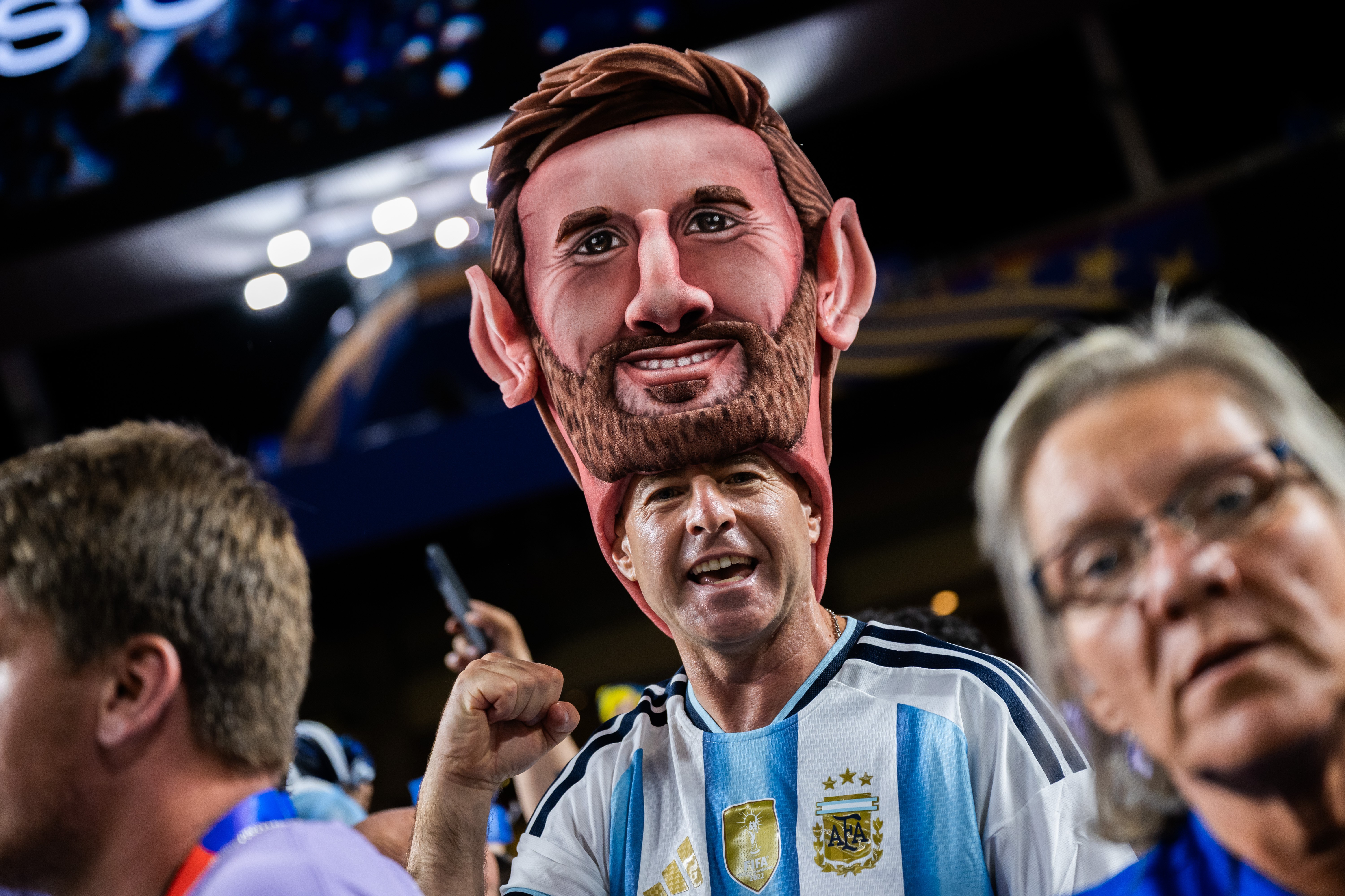 A soccer fan wears a huge sculpted foam head of Lionel Messi as a hat.