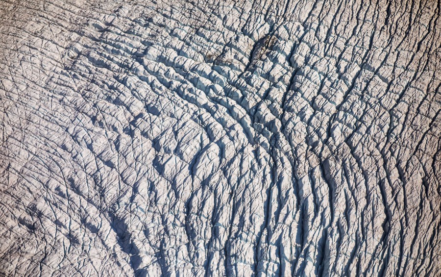 Cracks and criss-crossing crevasses are seen in a glacier's surface.