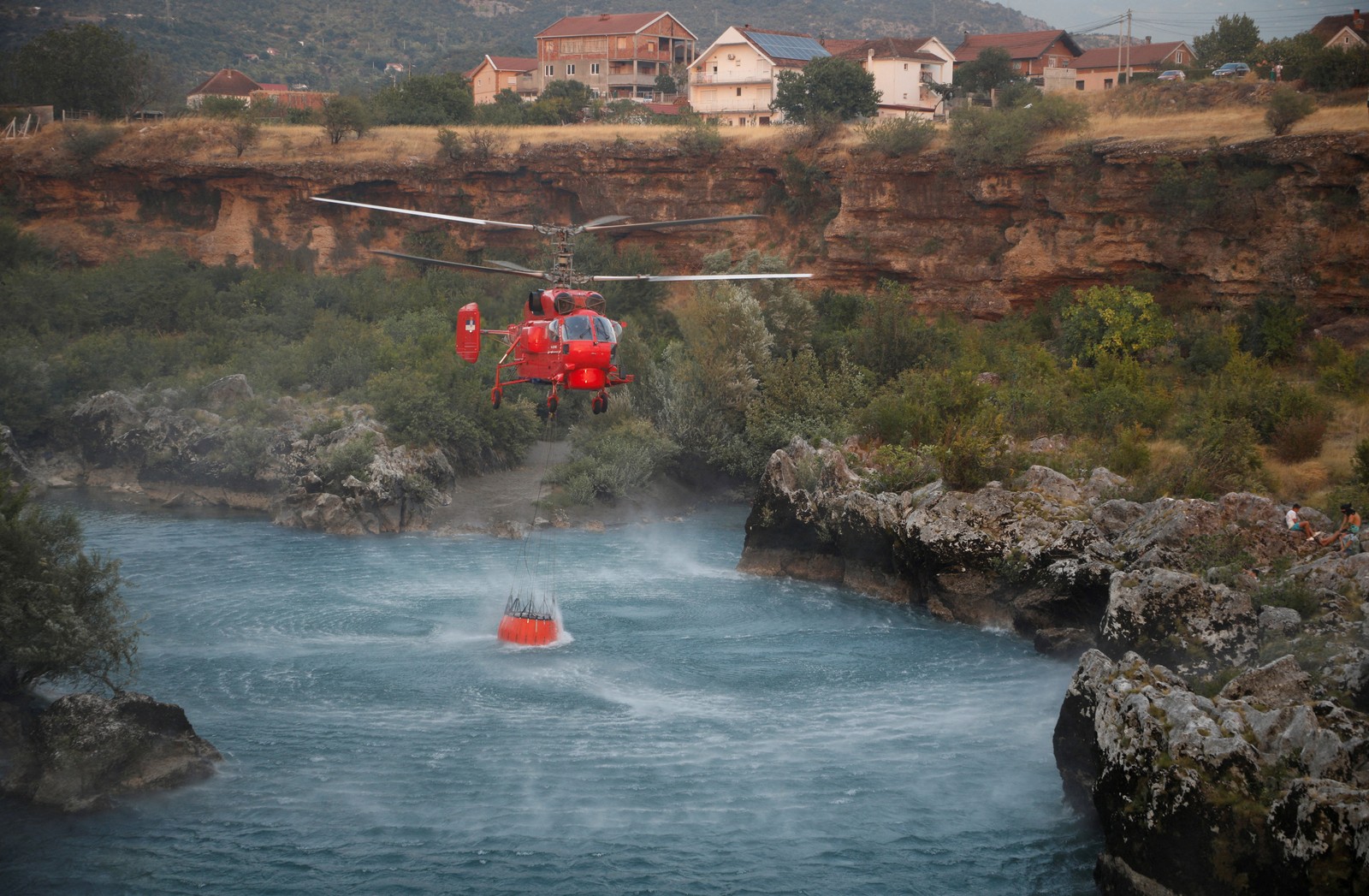 A firefighting helicopter collects water from a narrow river.
