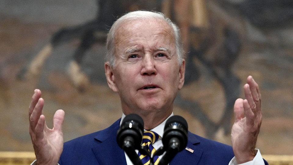 Joe Biden speaking in front of a microphone, hands raised