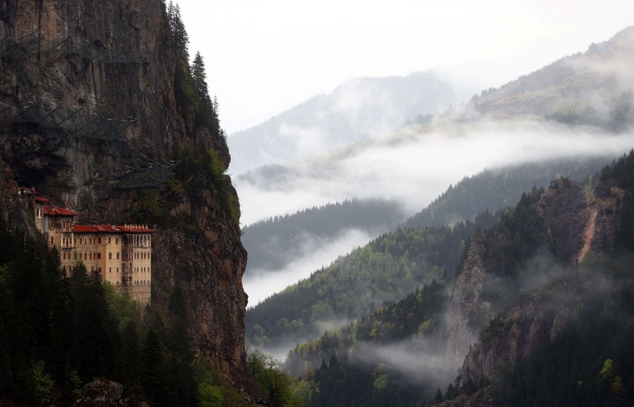 A view of a steep mountain valley, with a historic cliffside monastery visible at left.