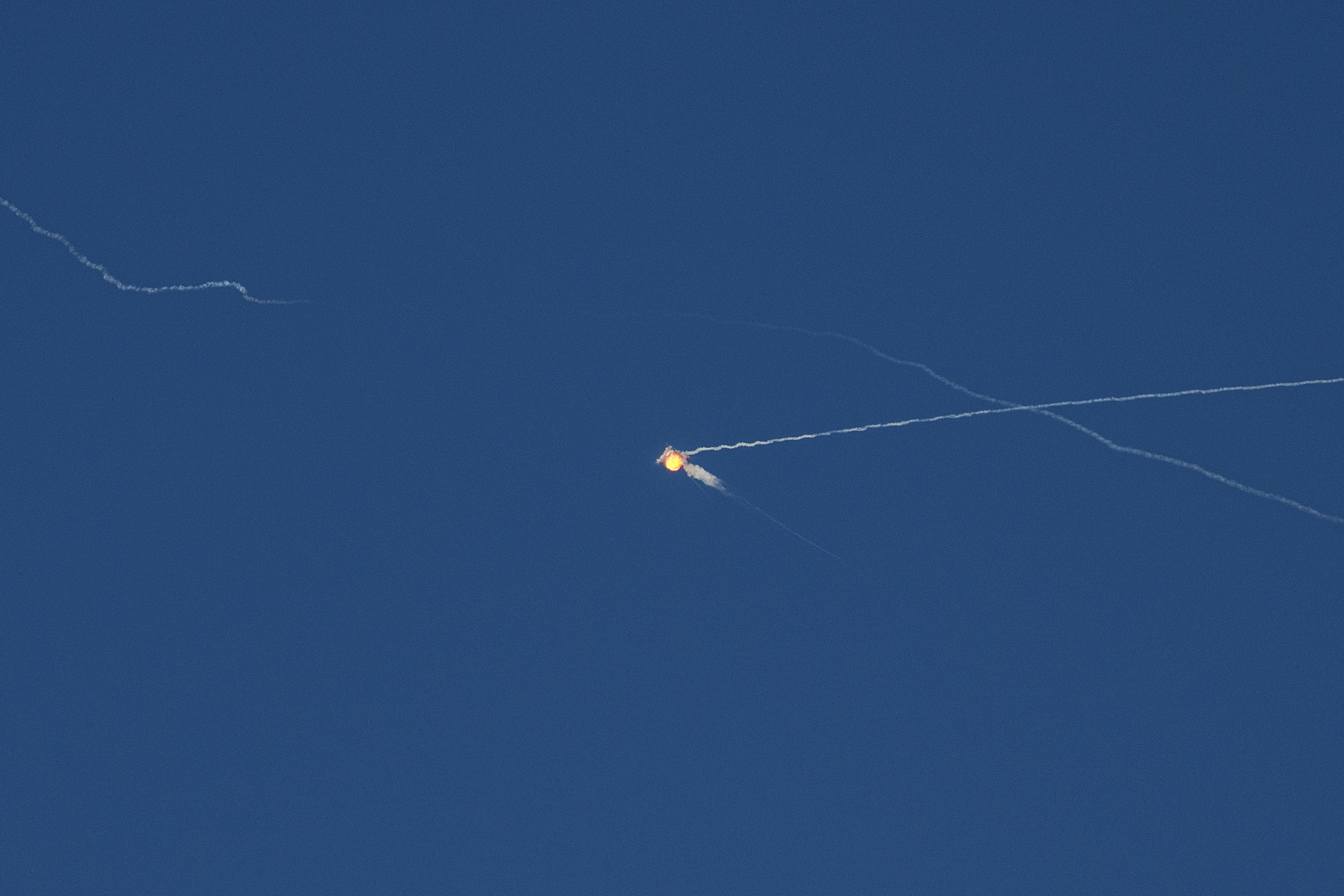 A rocket intercepts a ballistic missile, seen as a small explosion high in a blue sky.