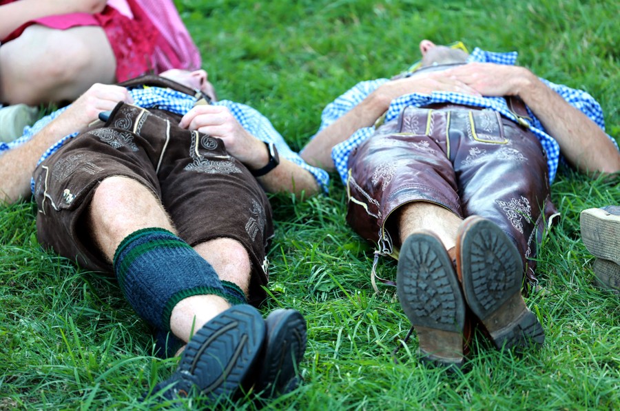 People in traditional Bavarian clothes lie on their backs on a patch of grass.